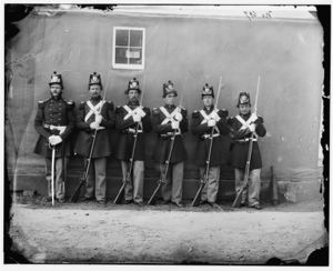 black & white photograph of six Marines standing in line, five with Civil War-era rifles and one with an NCO sword.