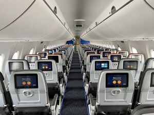 The inside of a plane is shown, with two seats per row on the left and three seats per row on the right. Each seat also has a personal television screen in front of it. The overall color scheme is gray.