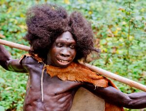 A smiling young boy with dark skim in loose clothing holding a spear