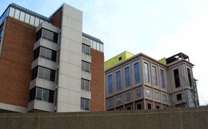 Two towers, one dark red brick, one half brick and half stone rise over a multi-story parking garage.