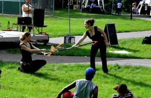 Two young persons seated on the ground watching two women dancing with fire