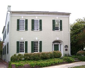 A two-story brick building with large windows and shrubbery in front of it