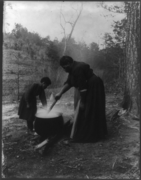 African American woman and child outdoors, standing by boiling cauldron of water, c. 1901.