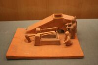 A Han-dynasty pottery model of two men operating a winnowing machine with a crank handle and a tilt hammer used to pound grain.