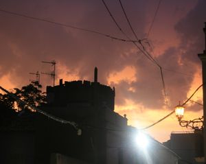 Coria sunset after rain. Sun is setting behind black silhouette of castle; and it lights heavy dark clouds from below