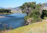 A river flows through an arid valley with bankside trees visible in the foreground