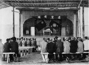 Soldiers and other sitting on benches in front of a stage
