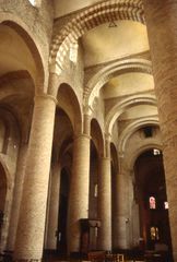A church interior of yellow stone with arches of alternation red and cream crossing the nave to support an unusual vaulting system.