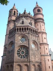 The apsidal end of a tall red stone church framed by circular towers.