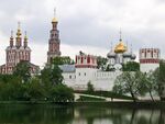 A walled monastery with red and white towers with golden domes