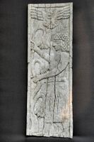 Standing man holding branches of lotus flowers. The winged god Assur appears above.