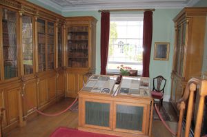 Photograph of a laboratory, with glass-encased, wooden bookcases on two walls and a window on the third. There is a display case in the middle of the room.