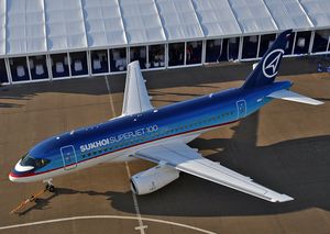 Top view of mostly blue twin-engine small jet airliner parked on ramp next to building.