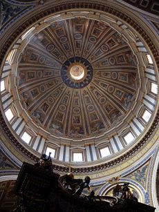 Photo looking up at the dome's interior from below. The dome is decorated at the top with a band of script. Around its base are windows through which the light streams. The decoration is divided by many vertical ribs which are ornamented with golden stars.